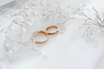 Obraz na płótnie Canvas два золотых обручальных кольца со свадебными украшениями невесты на белом фоне