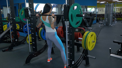 Fototapeta na wymiar Beautiful girl exercising squatting with barbell. Sportive woman doing squatting with a barbell at the gym. Fit woman doing squat with barbell in the gym closeup