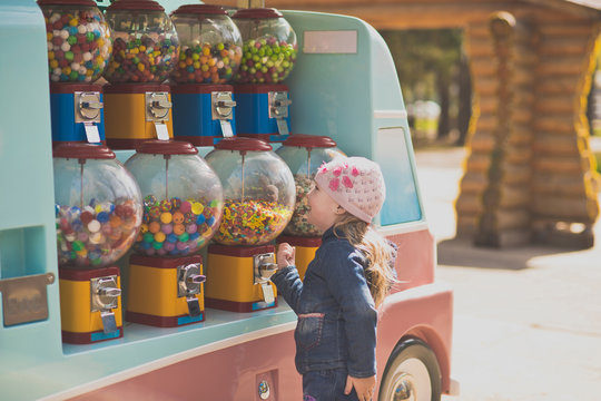 The little girl stopped in front of a battery of machines for the sale of small sweets. Genuinely enjoys opportunities to choose any treat Portrait of a girl in the Park on a walk.