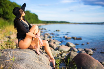 Fototapeta premium vacation concept - young beautiful woman in bikini sitting on rocky beach