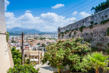 Fototapeta na wymiar Panoramic view of Rethymno from the Venetian Fortress (Fortezza) with rooftops and mountains in the background against the blue sky. Rethymno, Crete, Greece