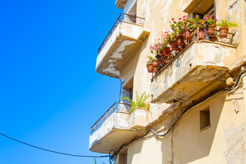Shabby but picturesque balcony of an old house decorated with pink flowers in the pots against the blue sky in the old town of Rethymno, Crete, Greece