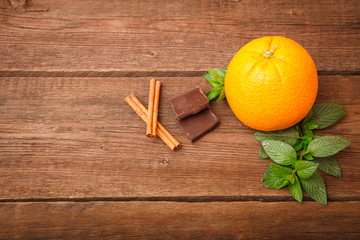 Fototapeta na wymiar Fresh orange with melissa, chocolate and cinnamon on a wooden background. Space for text. Background.