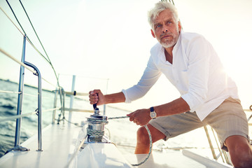 Mature man using a winch while sailing on the ocean