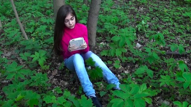 Beautiful teenager girl with tablet computer sits on the grass in Park. Movie of static camera.