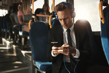 Young businessman wearing headphones and reading texts on a bus