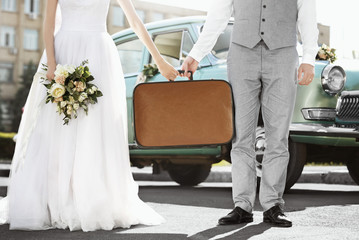 Happy wedding couple with suitcase and car outdoors