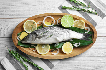 Wooden dish with fresh fish and slices of lemon on table