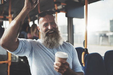 Mature man with a long beard laughing and drinking a takeaway cupe of coffee while standing on a...