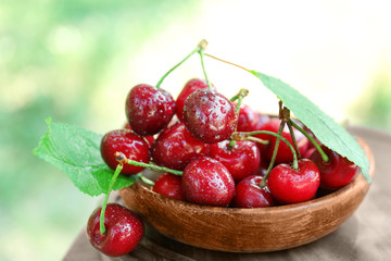 Wooden bowl with tasty ripe cherries on table outdoors