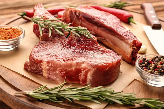 Fresh raw meat with rosemary on wooden board, close up