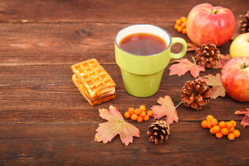 autumn composition. still life. berries of mountain ash, pine cones, fallen leaves and a cup of tea on a background of wood.