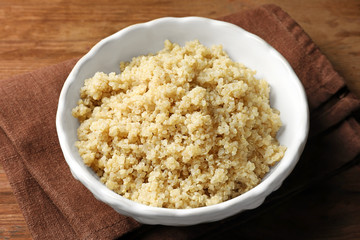 Bowl with boiled white quinoa grains on wooden table
