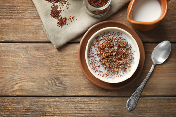 Bowl with boiled quinoa grains and milk on wooden table
