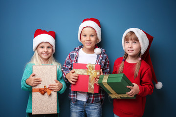 Cute little children with Christmas presents on color background