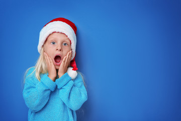 Cute girl in Santa hat on color background