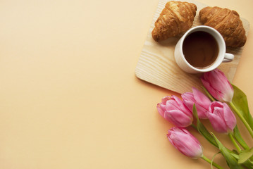 Coffee mug, сroissants, pink tulips on a peach background with the place for your text. Breakfast composition. Flat lay