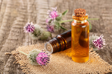 Fototapeta na wymiar burdock oil in glass bottle and burdock flowers on an old wooden background