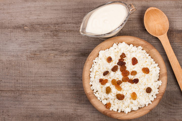 Cottage cheese in bowl with sour cream and raisins on old wooden background with copy space for your text. Top view
