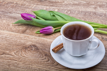 A cup of tea with cinnamon and purple tulips