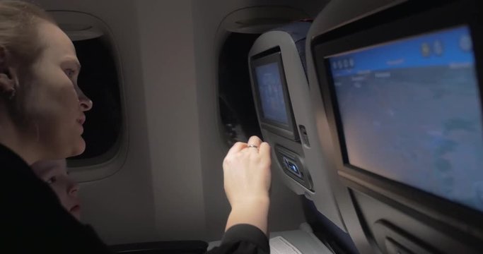 Mother and son traveling by air at night. Woman explaining to the child how to use touchscreen seat monitor in plane