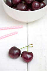 Fresh ripe black cherries in a white bowl on a white wooden background top view. Flat lay.