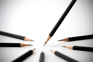Black pencil standing out from crowd of plenty identical black fellows on white table. Leadership, uniqueness, independence, initiative, strategy, dissent, think different, business success concept.