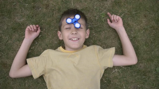 Happy boy twists the spinner on head and lies on grass Outdoors