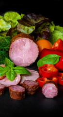 Smoked sausage, ham with red and green peppers and herbs on a dark background