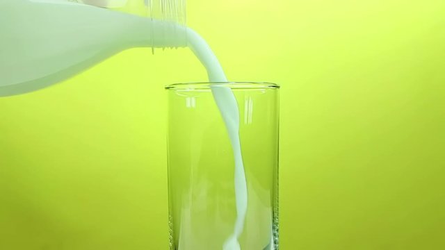 fresh white milk pouring into drinking glass on yellow gold background, shooting with slow motion, diet and healthy nutrition concept