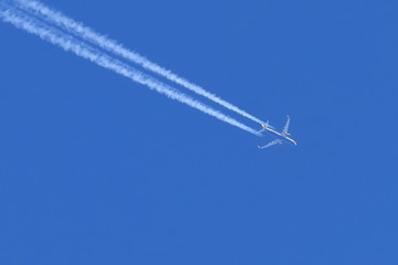 Jet plane pulling white contrails in clear blue sky. Airliner trail while transports passengers.