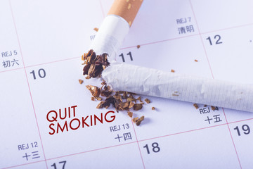 Quit Smoking word on calender sheet with broken cigarette. Concept of choosing a day to quit smoking