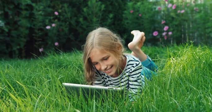 Cheerful girl using tablet pc and lying in grass. Dolly shot