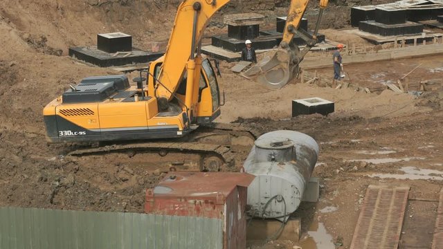 Large construction of large complex of buildings. Yellow excavator on a construction site in the summer season