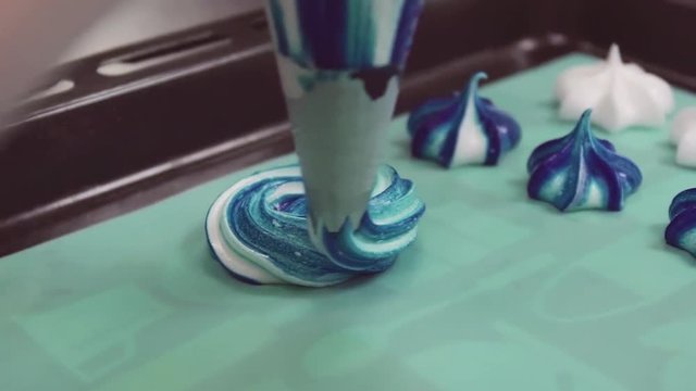 Colorful blue and white cream swirl squized from pastry bag on green cooking paper in baking tray with merengues