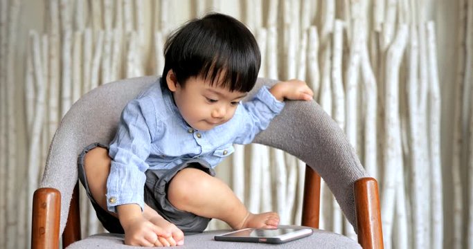 Little boy watching on cellphone and sitting on chair
