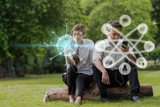 Happy Asian Couple Using And Listening The Song And Using The Social Network Via Smart Mobile Phone For Online Shopping With Omni Channel In The Park, Lifestyle And Technology Concept