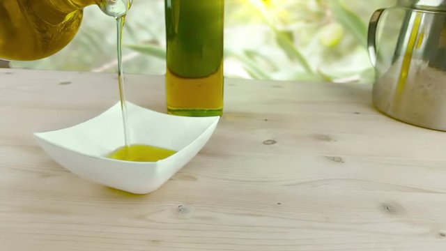 pouring cooking olive oil in the bottle in the white container on wood table background near olive oil bottle, shot in slow motion in outdoor, concept of healthy food diet and nutrition