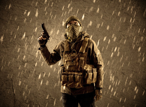 Dangerous heavily armed terrorist soldier with mask on grungy rainy background