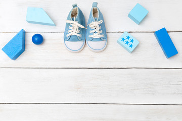Boyâ€™s blue shoes and toys on a white wooden background. View from above