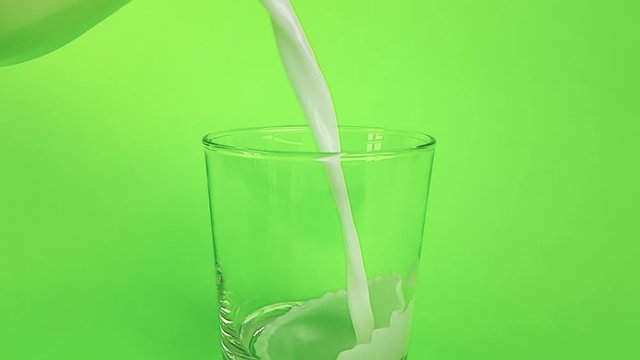 fresh white milk pouring into drinking glass on chroma key green screen background, shooting with slow motion, diet and healthy nutrition concept