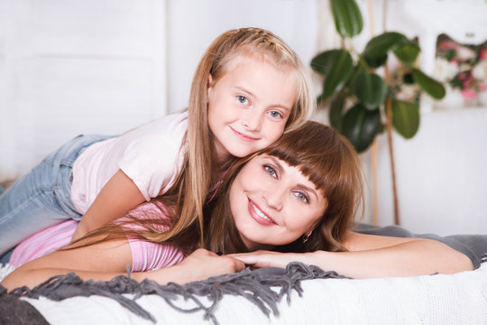 Portrait of beautiful mother and her daughter hugging in a bed, looking at camera. Happy family.
