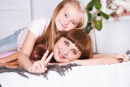 Portrait of beautiful mother and her daughter hugging in a bed, looking at camera. Happy family.
