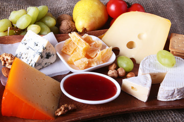 Assortment of cheese with fruits, grapes and nuts on a wooden serving tray.