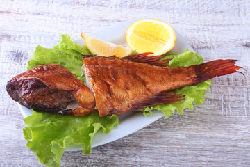 Smoked fish and lemon on green lettuce leaves on Wooden cutting board isolated on white background.