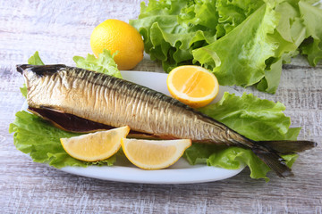 Smoked mackerele and lemon on green lettuce leaves on Wooden cutting board isolated on white background.