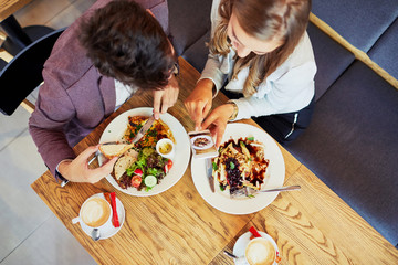 Cute young couple eating together and taking photos of their food in a restaurant