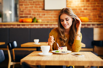 Beautiful young woman sitting at table in cafe and eating cake