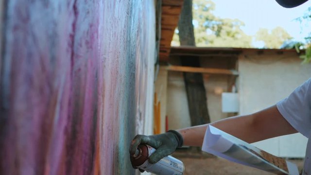 Street artist painting colorful graffiti on generic wall - Modern art concept with urban guy performing and preparing live murales with red aerosol color spray. Slow motion.