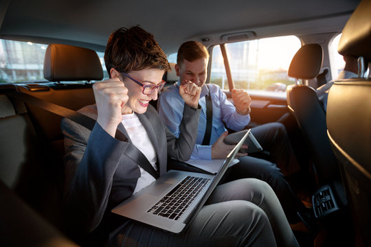 Excited businesspeople looking at laptop in car on trip.